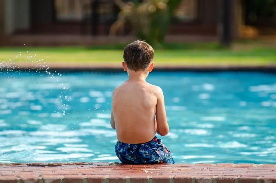 Child sitting at the edge of a backyard swimming pool