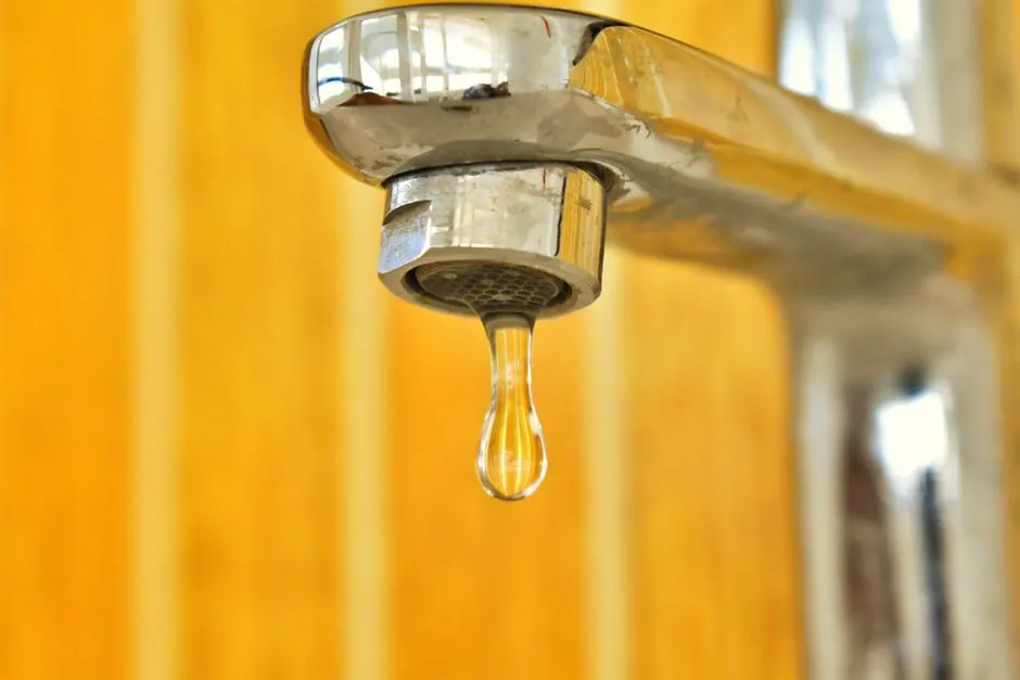 Water droplet forming on a dripping brass faucet