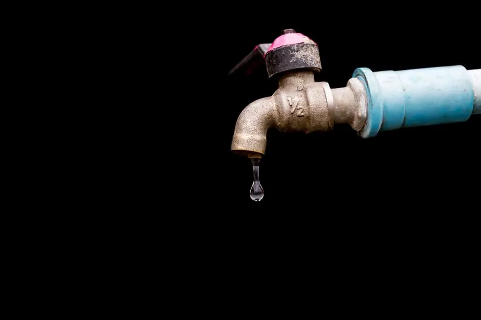Dripping spigot connected to a blue hose against a dark background