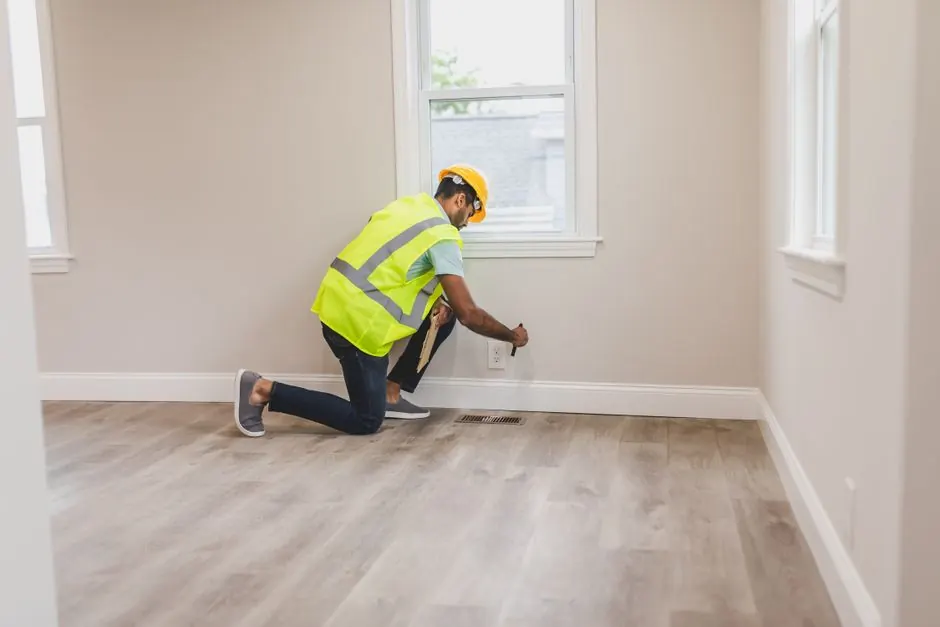 Inspector in a high-visibility vest checking a baseboard in an empty room