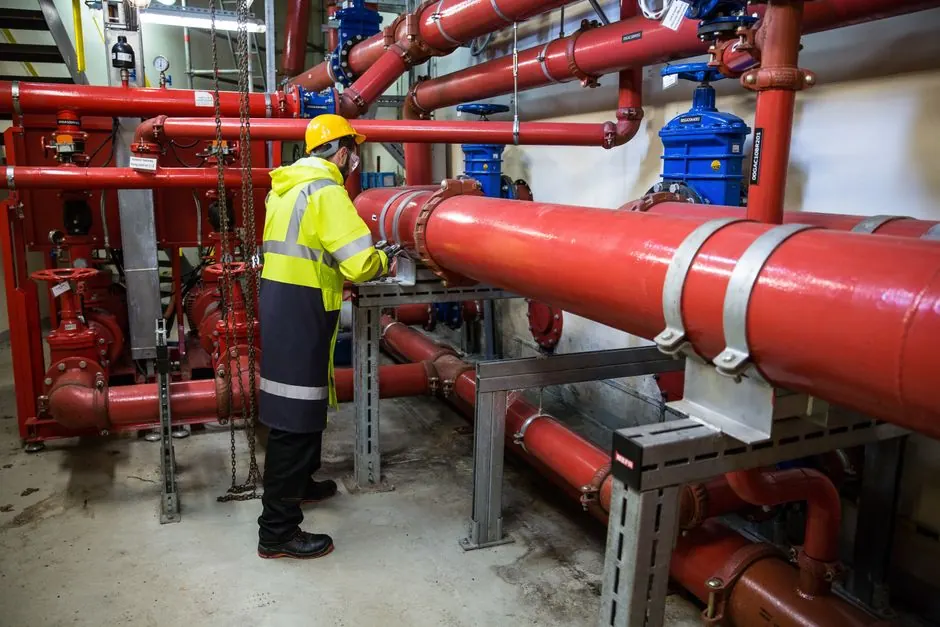 Engineer in safety gear inspecting large red water pipes