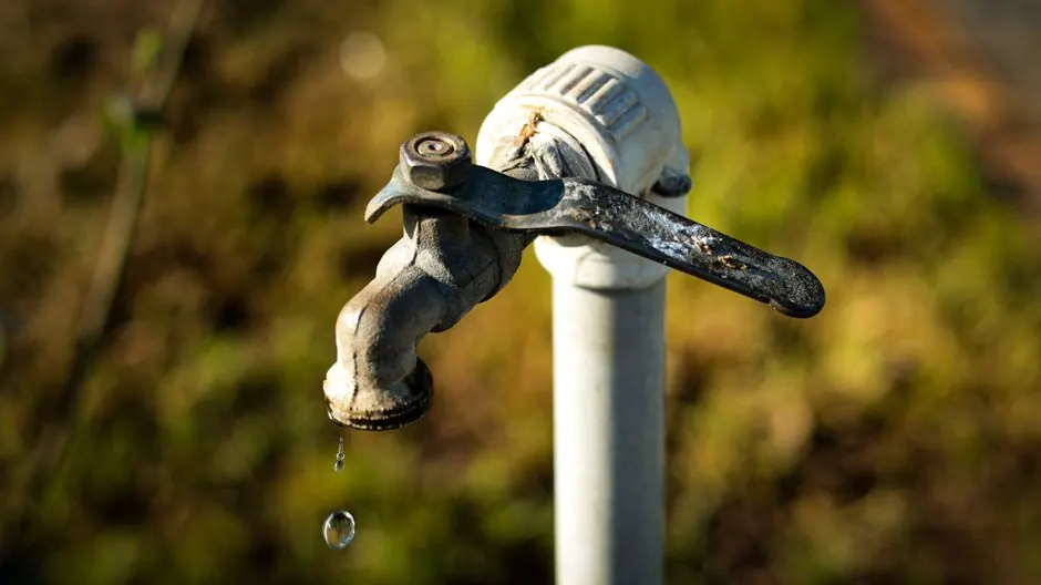 Weathered garden tap dripping beside a white pipe