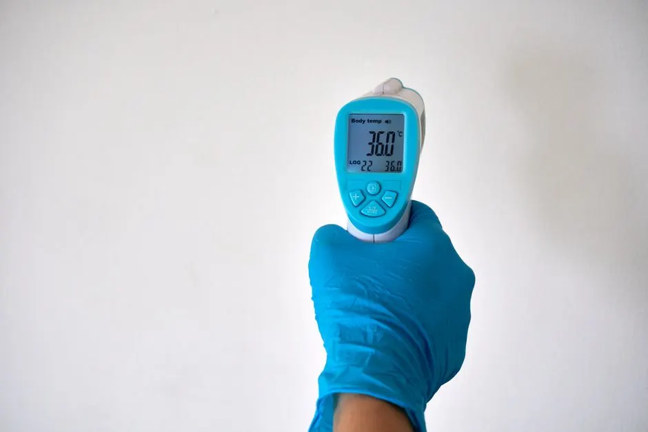 Gloved hand holding an infrared thermometer against a wall